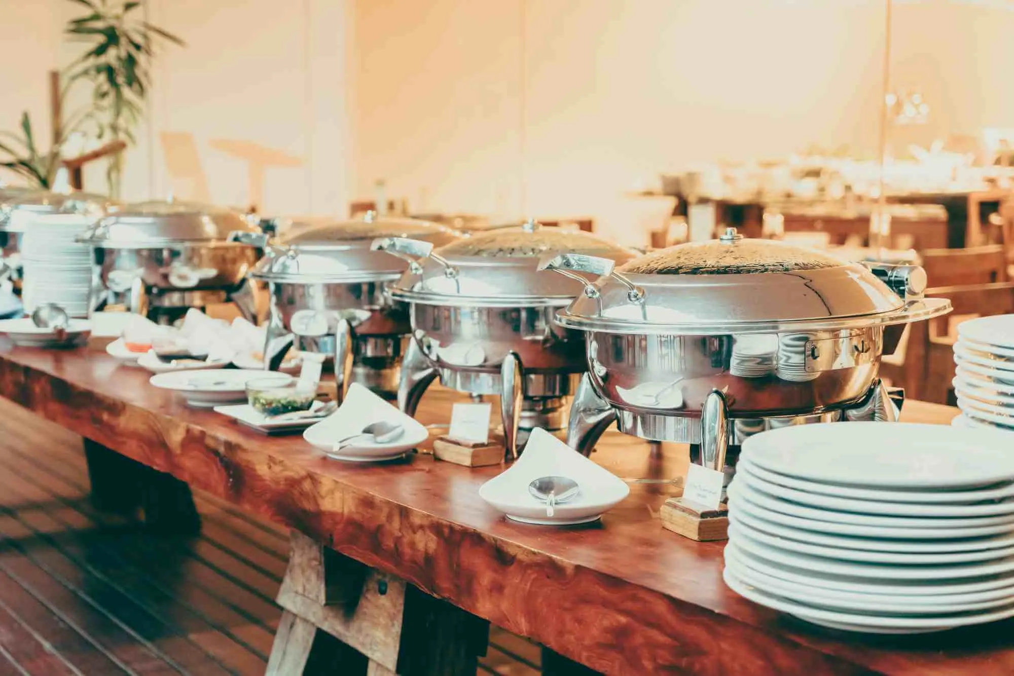 A row of steel chafing dishes and stacked plates on a buffet table